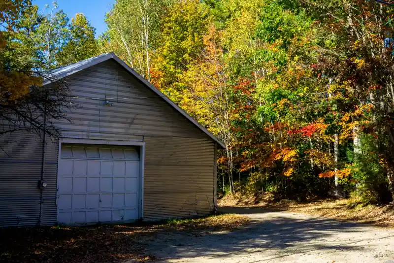 Metal garage building with a roll-up door beside fall trees